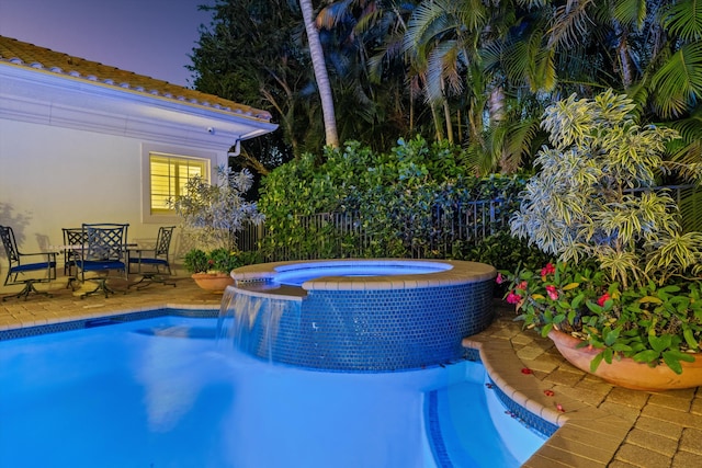 pool at dusk featuring a patio area and an in ground hot tub