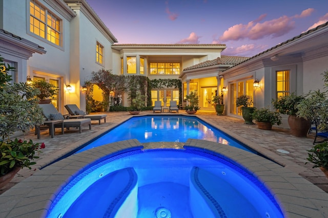 pool at dusk with an in ground hot tub and a patio area