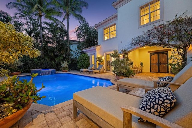 pool at dusk featuring an in ground hot tub, a patio, and french doors