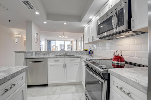 kitchen with a tray ceiling, kitchen peninsula, white cabinets, stainless steel appliances, and backsplash