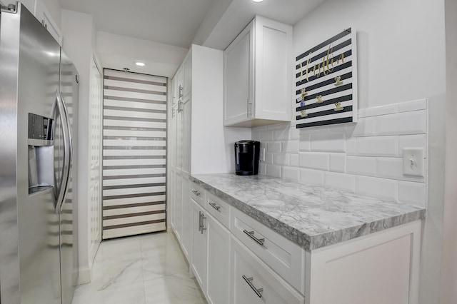 kitchen featuring tasteful backsplash, stainless steel fridge, light stone counters, and white cabinets