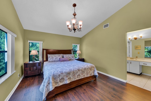 bedroom with an inviting chandelier, ensuite bath, vaulted ceiling, and hardwood / wood-style floors