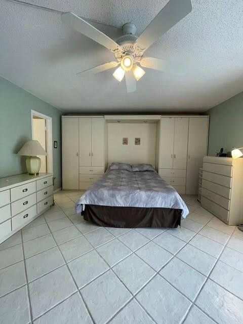 bedroom with ceiling fan, light tile patterned floors, and a textured ceiling