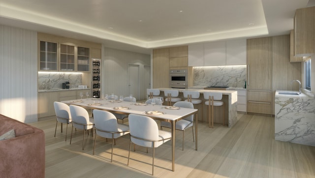 dining area with a raised ceiling, sink, and light wood-type flooring