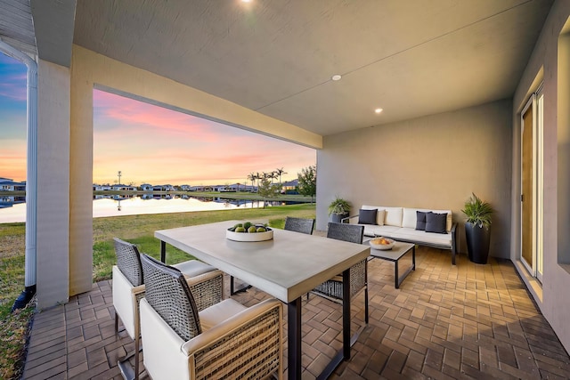 patio terrace at dusk with a water view, outdoor lounge area, and outdoor dining space