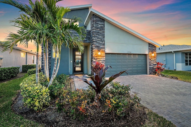 view of front facade featuring stone siding, decorative driveway, an attached garage, and stucco siding