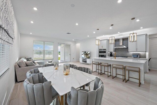 kitchen featuring appliances with stainless steel finishes, decorative light fixtures, sink, a kitchen island with sink, and wall chimney range hood