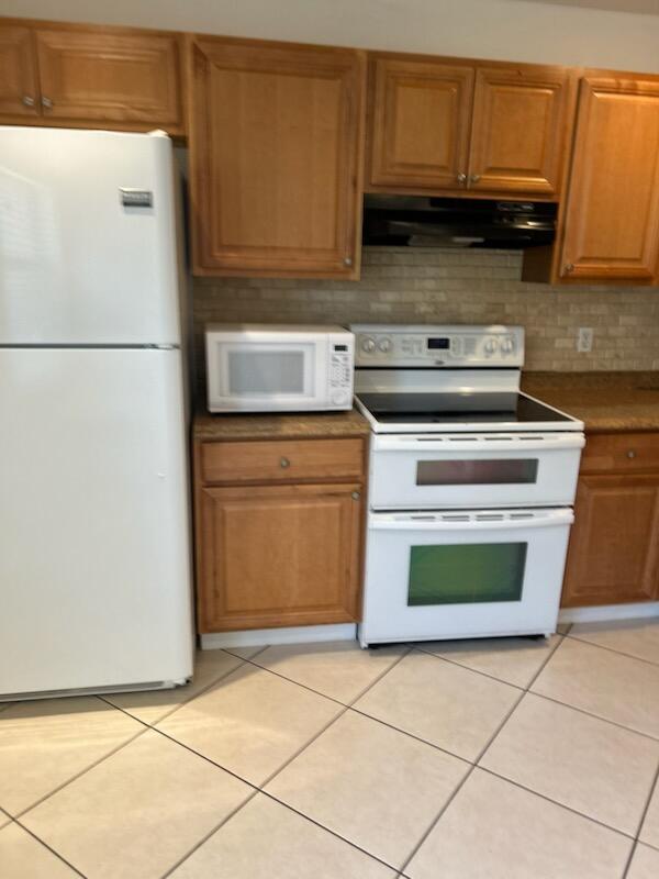 kitchen featuring backsplash, white appliances, light tile patterned floors, and exhaust hood