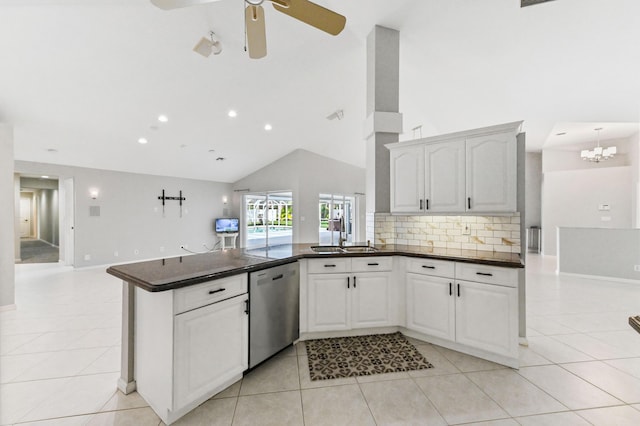 kitchen with a peninsula, stainless steel dishwasher, a sink, dark countertops, and high vaulted ceiling