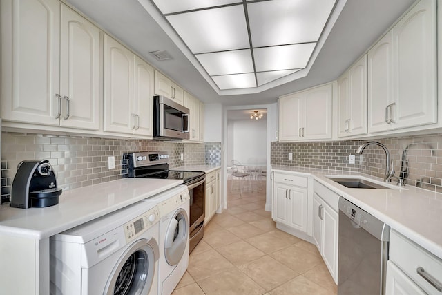 kitchen featuring appliances with stainless steel finishes, sink, white cabinets, light tile patterned floors, and washing machine and dryer