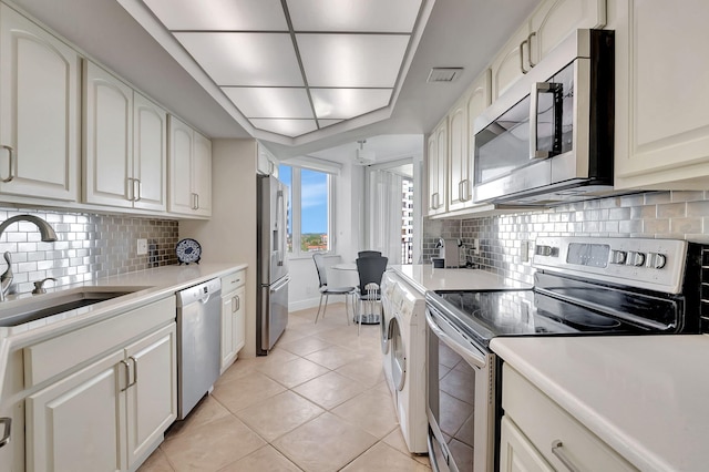 kitchen featuring sink, light tile patterned floors, appliances with stainless steel finishes, white cabinets, and backsplash