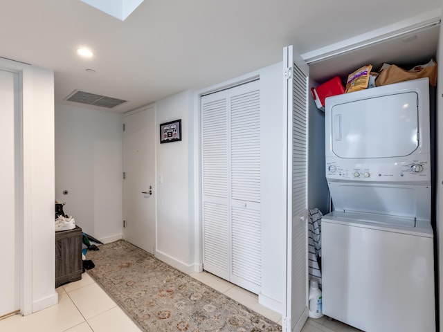 clothes washing area featuring light tile patterned flooring and stacked washer and clothes dryer