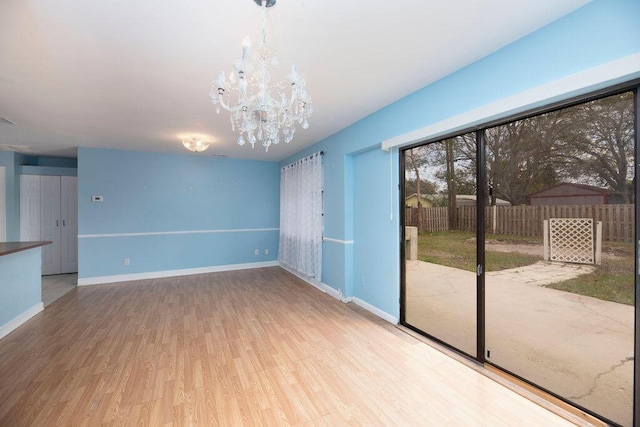 empty room featuring a notable chandelier and light wood-type flooring