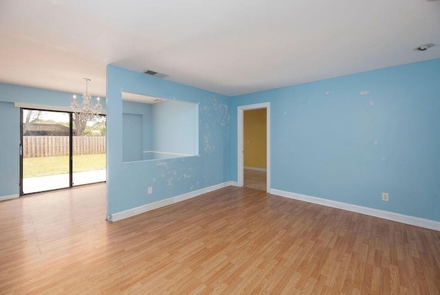 spare room with a notable chandelier and light wood-type flooring