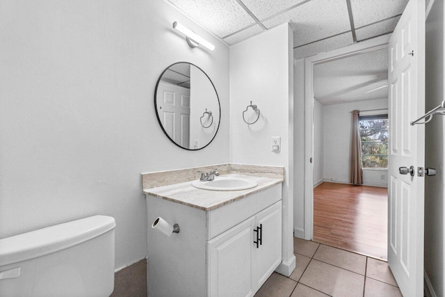 bathroom featuring tile patterned floors, toilet, vanity, and a drop ceiling