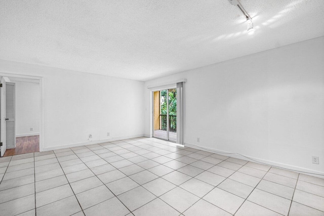 tiled spare room with rail lighting and a textured ceiling