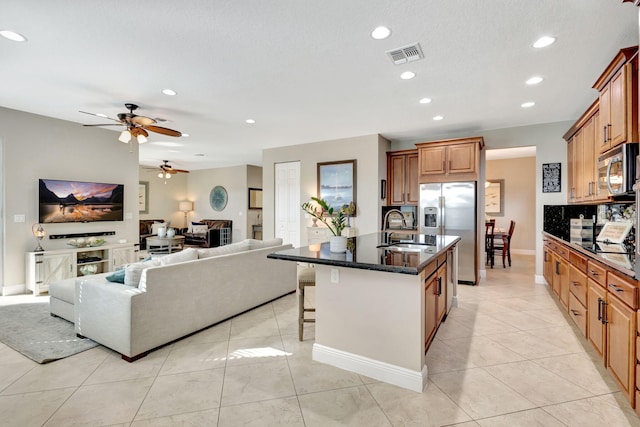 kitchen with appliances with stainless steel finishes, sink, a kitchen breakfast bar, light tile patterned floors, and a center island with sink