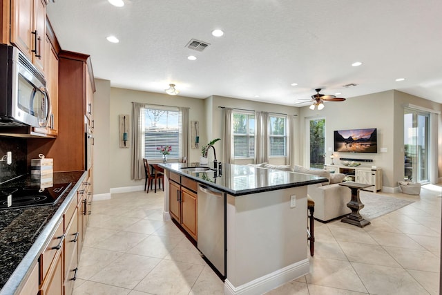 kitchen featuring an island with sink, sink, dark stone counters, light tile patterned floors, and stainless steel appliances