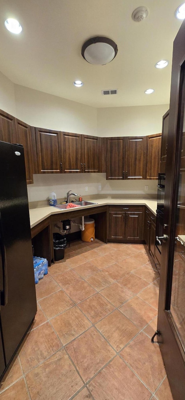 kitchen with light tile patterned flooring, dark brown cabinetry, sink, and black appliances