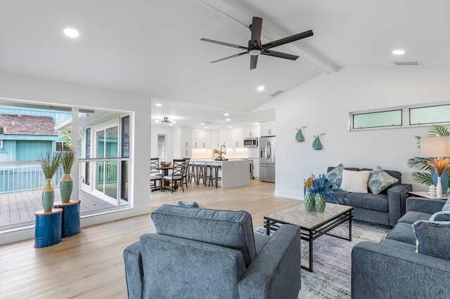 living room featuring light wood-style floors, visible vents, and vaulted ceiling with beams