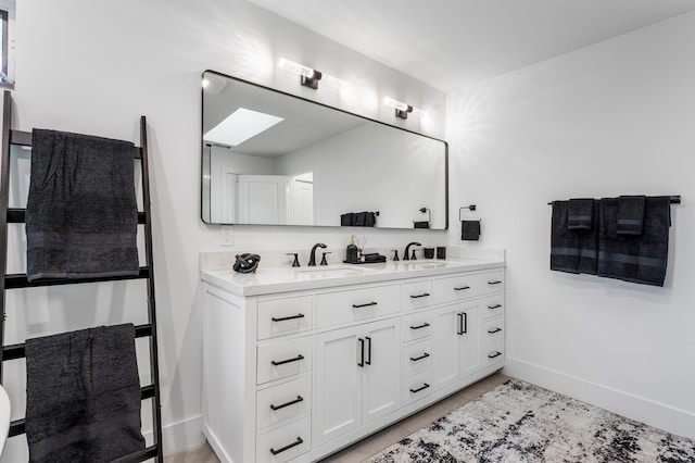 full bath with a skylight, a sink, baseboards, and double vanity