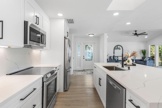 kitchen featuring visible vents, white cabinets, light stone countertops, stainless steel appliances, and a sink