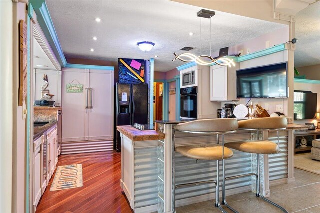 kitchen with pendant lighting, hardwood / wood-style floors, a textured ceiling, and black appliances