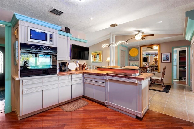 kitchen with visible vents, oven, ceiling fan, a peninsula, and wood finished floors