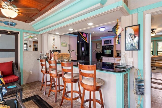 bar with sink, beam ceiling, black appliances, and ceiling fan