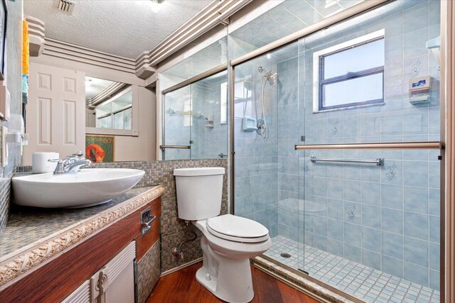 bathroom with hardwood / wood-style flooring, vanity, a textured ceiling, a shower with shower door, and toilet