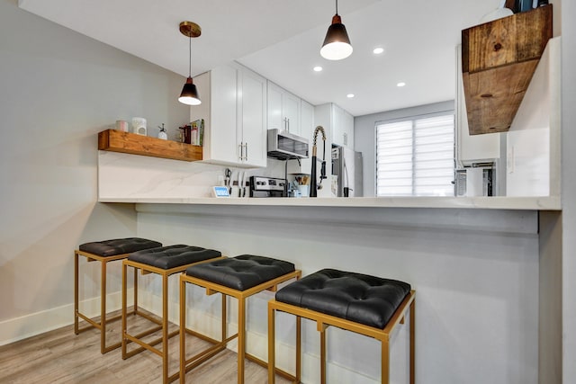 kitchen featuring stainless steel appliances, white cabinetry, light hardwood / wood-style flooring, and decorative light fixtures