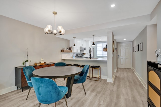 dining area with sink, a chandelier, and light wood-type flooring