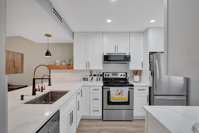 kitchen featuring appliances with stainless steel finishes, pendant lighting, white cabinetry, sink, and light stone counters