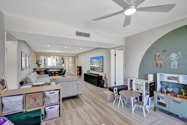 living room featuring sink, ceiling fan with notable chandelier, and light hardwood / wood-style flooring