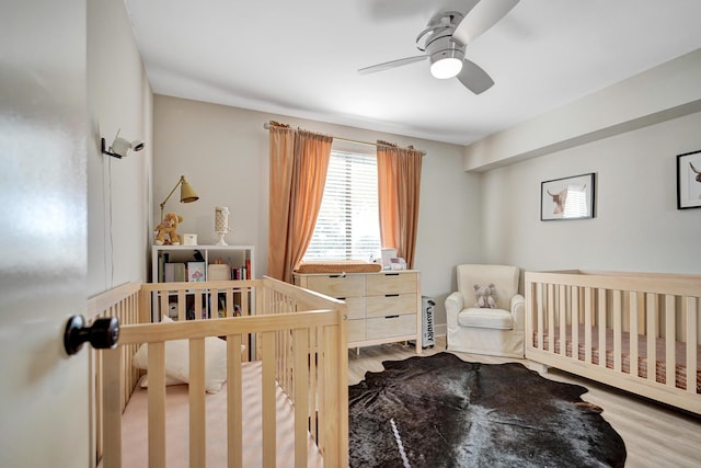 bedroom with ceiling fan, a nursery area, and light hardwood / wood-style floors