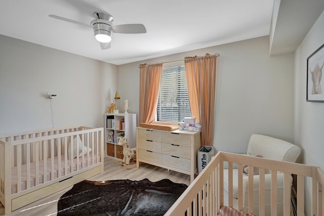 bedroom featuring light hardwood / wood-style flooring, a nursery area, and ceiling fan