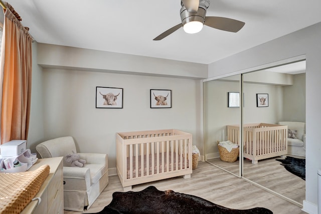 bedroom with a crib, ceiling fan, light wood-type flooring, and a closet