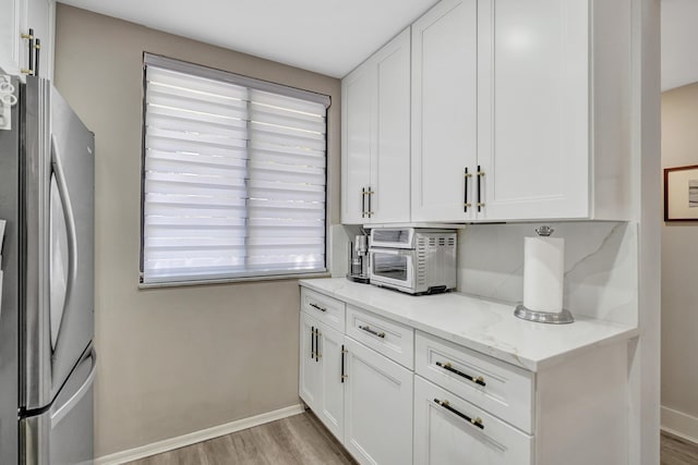 kitchen featuring white cabinets, light wood-type flooring, stainless steel fridge, and light stone counters