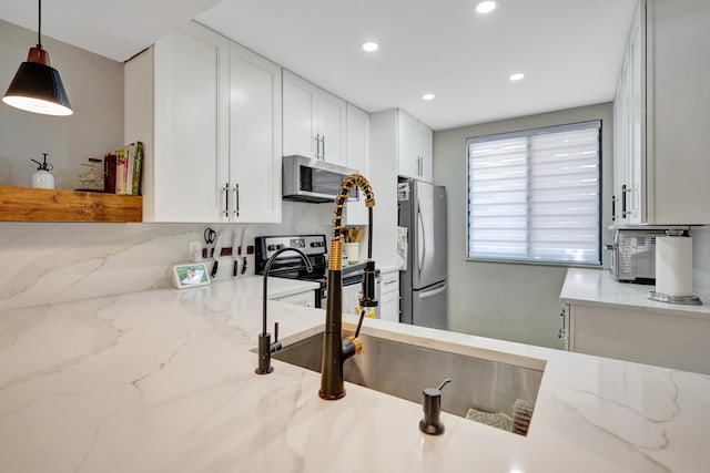 kitchen with white cabinetry, appliances with stainless steel finishes, decorative light fixtures, and light stone countertops