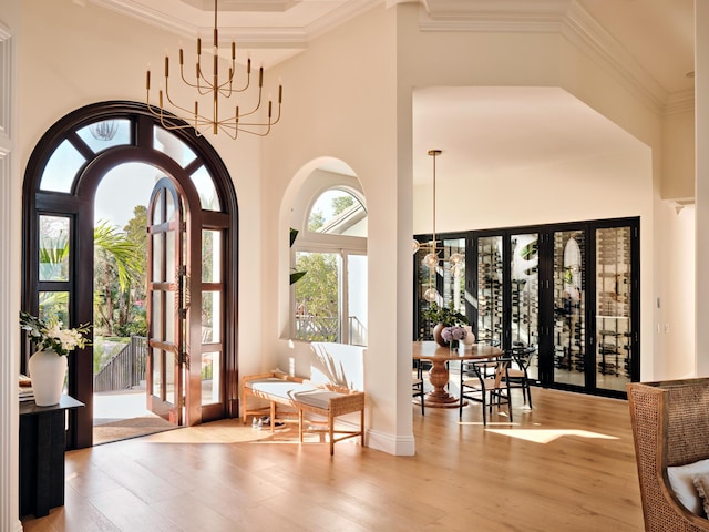 interior space with crown molding, an inviting chandelier, a high ceiling, french doors, and light wood-type flooring