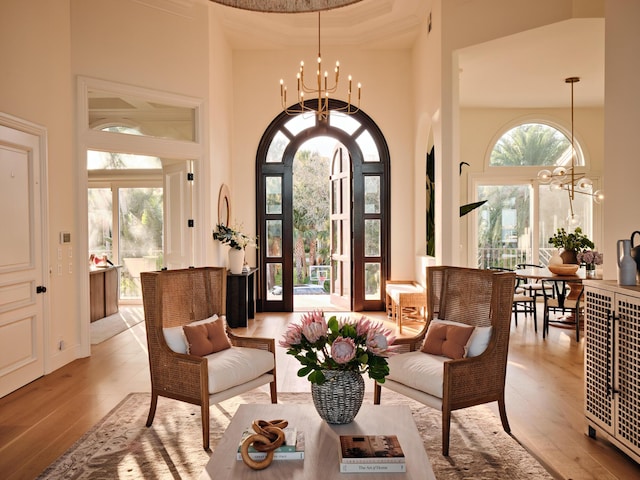 living area with an inviting chandelier, light wood-style flooring, a towering ceiling, and a healthy amount of sunlight