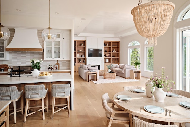 dining space featuring light wood-style flooring, a raised ceiling, a fireplace, and a notable chandelier