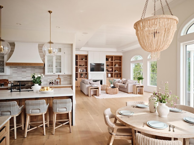 dining area with a tray ceiling, an inviting chandelier, light wood-style flooring, and a fireplace