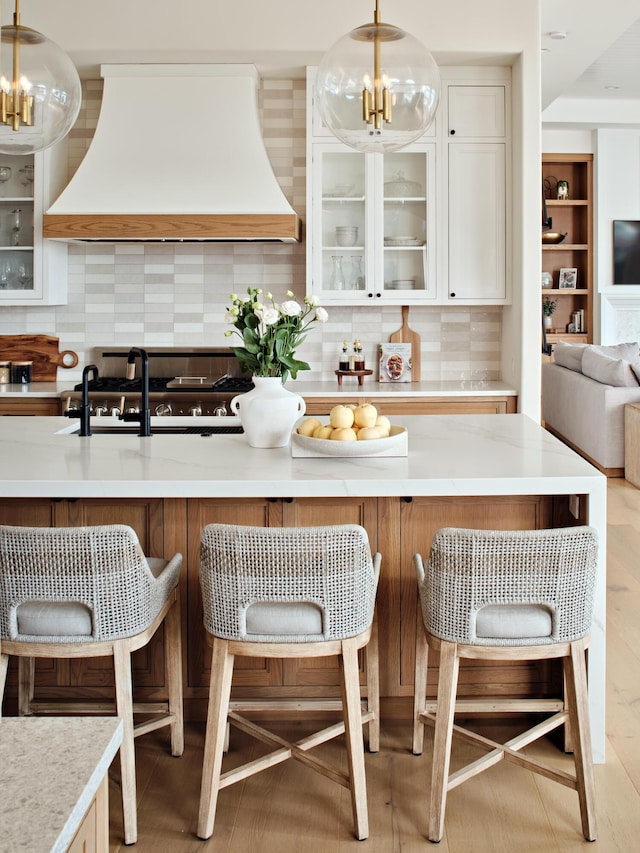 kitchen with an inviting chandelier, premium range hood, glass insert cabinets, and a kitchen bar