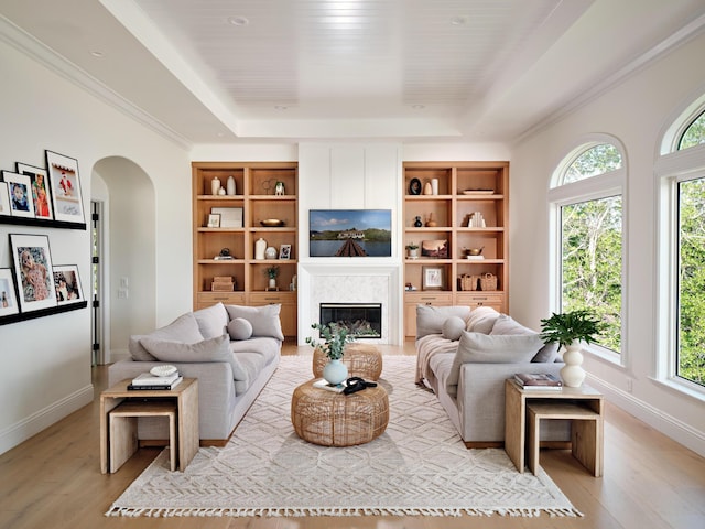 living room featuring built in shelves, a high end fireplace, a raised ceiling, and light hardwood / wood-style flooring