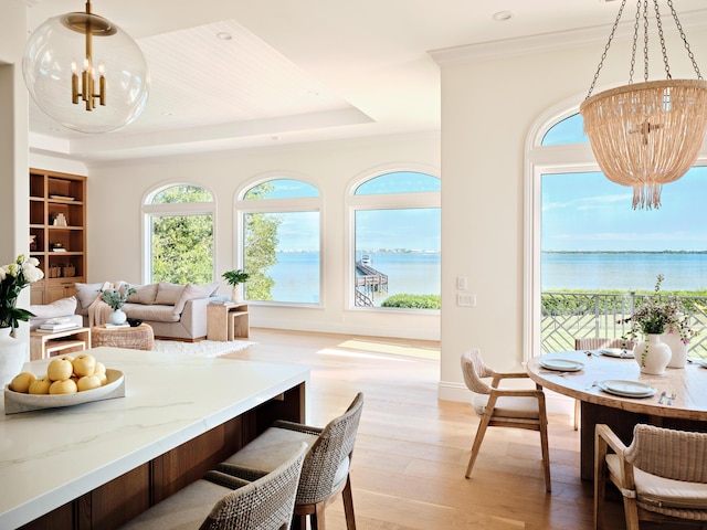 dining space with light wood-type flooring, a raised ceiling, a chandelier, and a water view