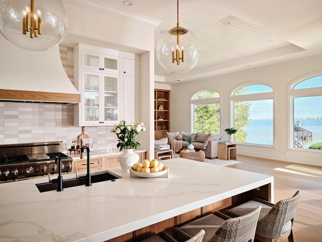 kitchen featuring premium range hood, a tray ceiling, decorative light fixtures, and light stone counters