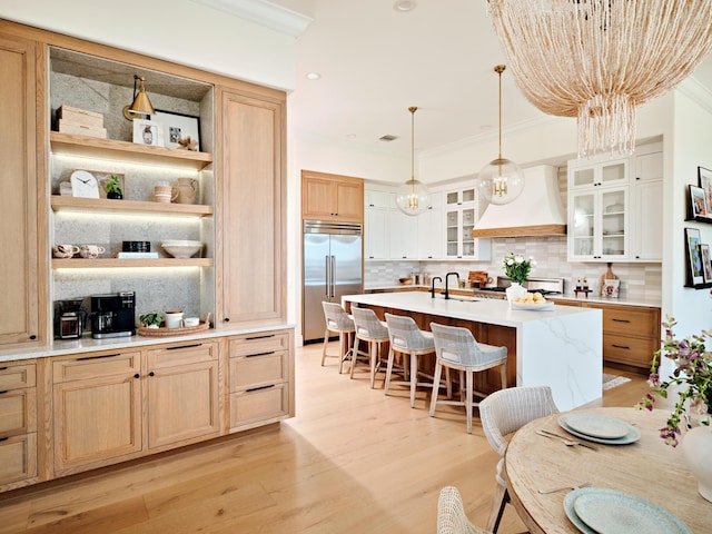 kitchen featuring sink, white cabinetry, custom range hood, an island with sink, and built in fridge