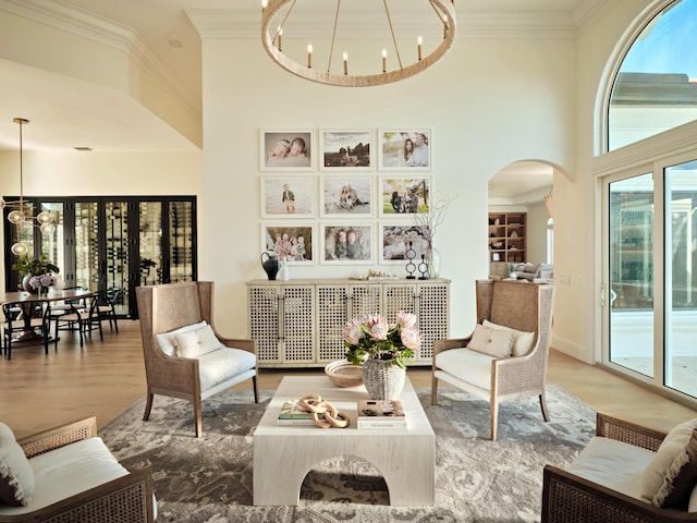 living area with a high ceiling, ornamental molding, wood-type flooring, and an inviting chandelier