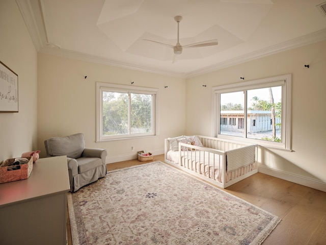 bedroom featuring a nursery area, ceiling fan, a tray ceiling, crown molding, and light wood-type flooring